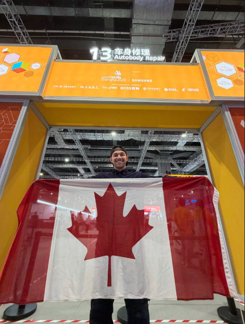 A photo of Team Canada and Ontario competitor, Ethan Almeida, holding the Canada flag outside the entrance to the Autobody Repair contest at World Skills Shanghai 2026.
